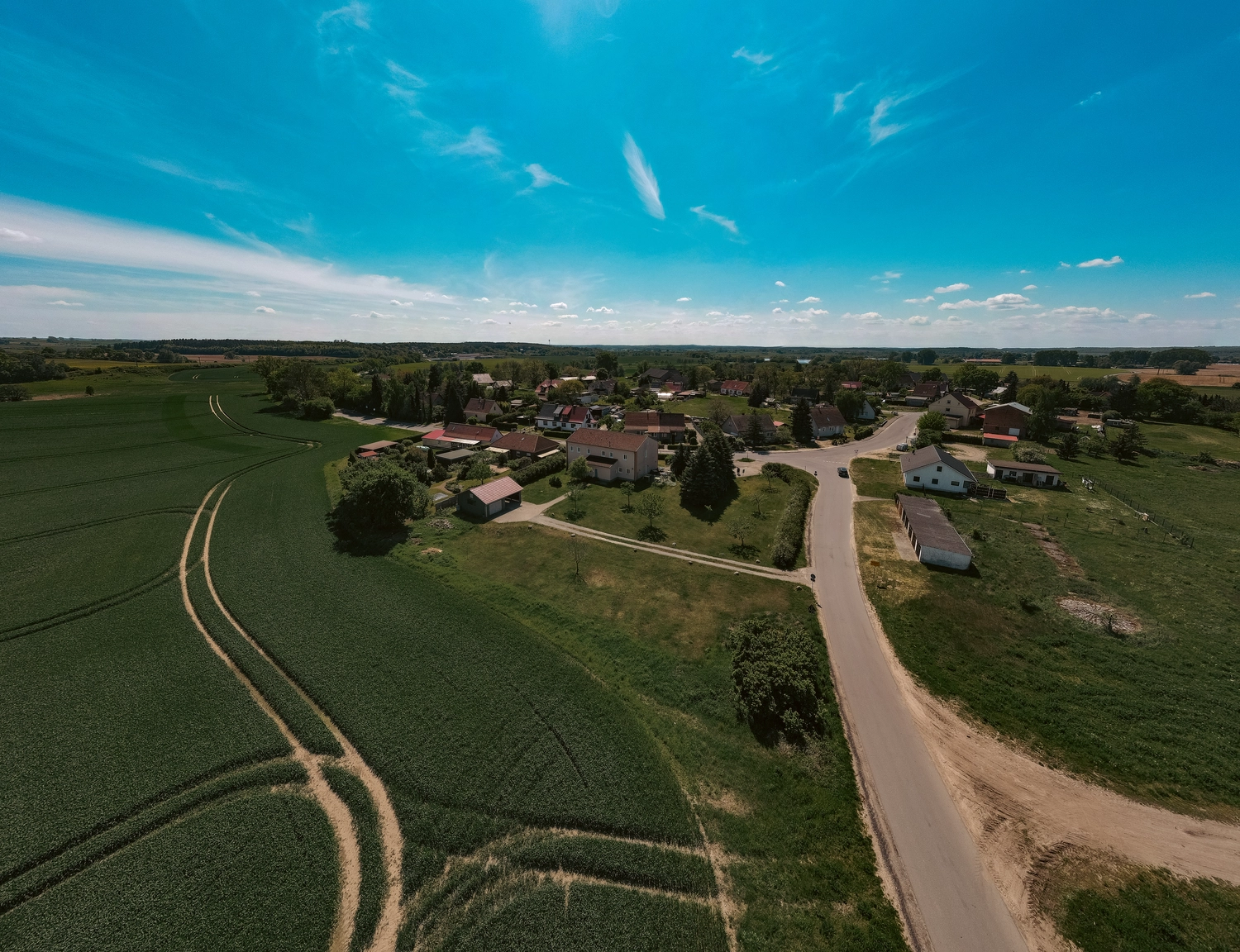 Erbkrug Blankensee -  Ferienapartments - Ein Luftpanorama eines ländlichen Dorfes, eingebettet zwischen weitläufigen landwirtschaftlichen Feldern unter einem strahlend blauen Himmel mit vereinzelten Wolken.